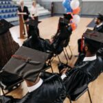 Group of students in caps and gowns attending a graduation ceremony indoors.